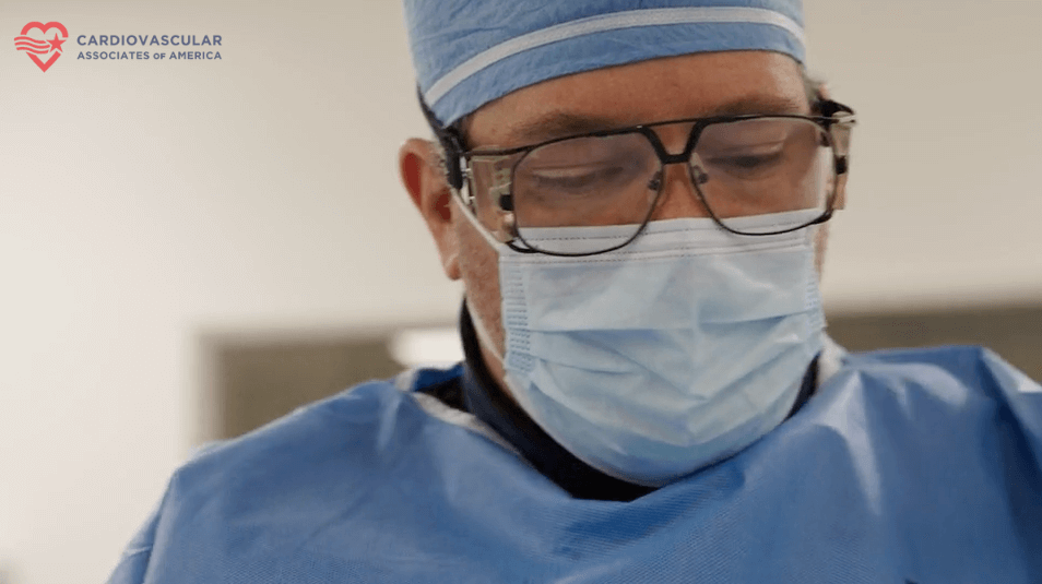 Surgeon in blue scrubs, mask, and glasses focused during a medical procedure